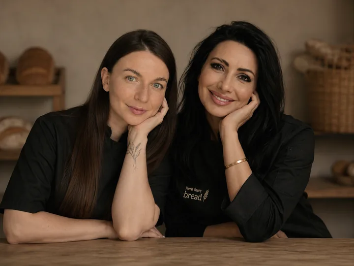 Anna and Maryna in black bakers' jackets, leaning on a wooden counter.