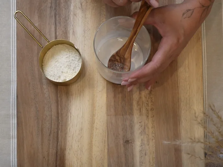 A hand stirring the jar, with a brass measure of bread flour beside it.