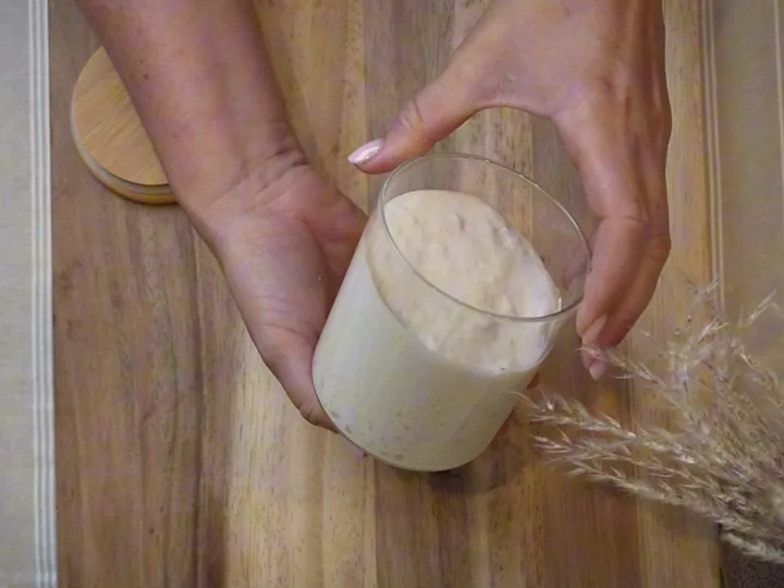 Two hands cupped around a glass jar of pale, risen sourdough starter.