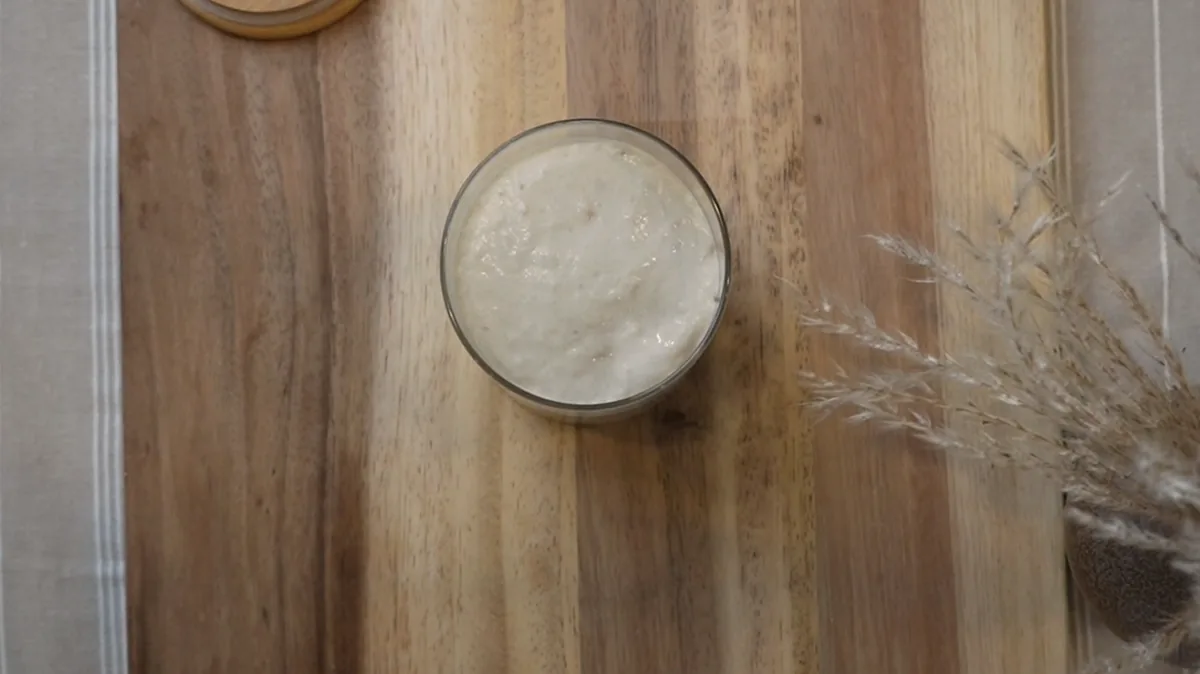 A jar of active sourdough starter on a wooden board, seen from above.